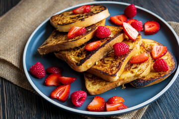 French toast on a plate with fresh strawberries and raspberries. Tasty morning breakfast or brunch with gluten free bread. Easy making and healthy dessert on a rustic cloth. Side view