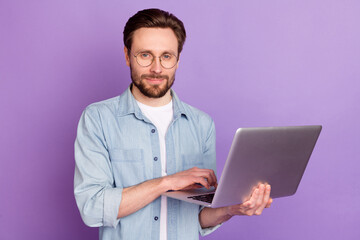 Photo of serious young man hold computer good mood wear glasses isolated on purple color background