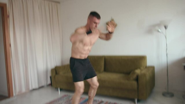 Handsome young bodybuilder with naked torso training at home on isolation during the coronavirus pandemic