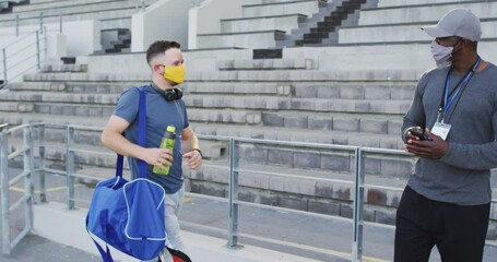 Diverse male coach and disabled athlete wearing face mask touching elbows before training session - Powered by Adobe