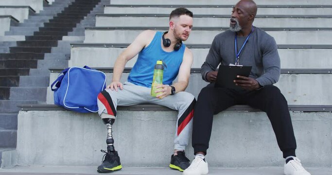 Diverse male coach and disabled athlete with prosthetic leg talking during training session