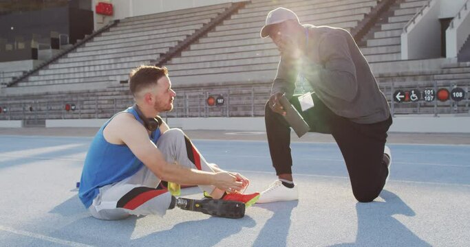Diverse male coach and disabled athlete with prosthetic leg talking during training session