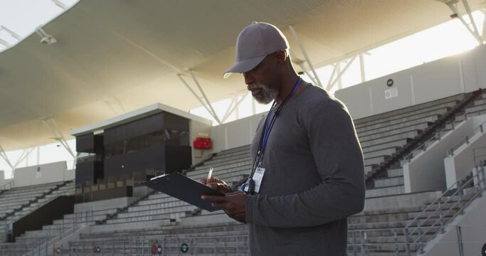 Smiling african american male coach making notes on sunny day