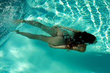 Woman swimming under water in a blue pool on early summer morning	