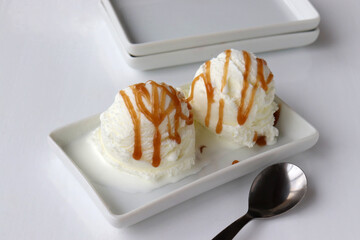Vanilla ice cream scoops with caramel topping on plate on white table background. Frozen yogurt with caramel syrup. Summer refreshing dessert. Top view