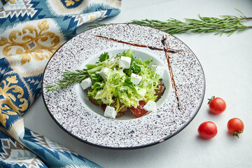 Mix salad with baked eggplant, tomatoes and feta cheese in a white plate on a white tablecloth