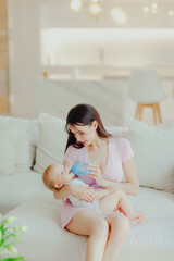 Young beautiful mother bottle feeding her little son at home