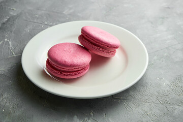 Appetizing almond flour Macaroon cookies with raspberries interlayer served in a white plate on a gray background