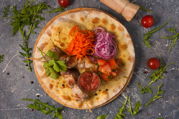 skewer of pork on pita bread with vegetables and tomato sauce. Top view