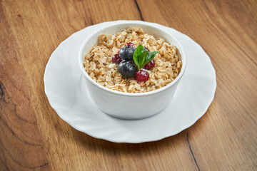 Appetizing oatmeal in milk with berries in a white bowl on a wooden background.