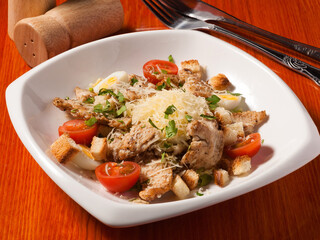 Caesar salad with chicken in a white plate on a wooden table