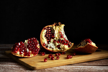 Dramatic style cut pomegranate, in the dark, on a cutting board, pomegranate chunks, front view, red seeds scattered, front view