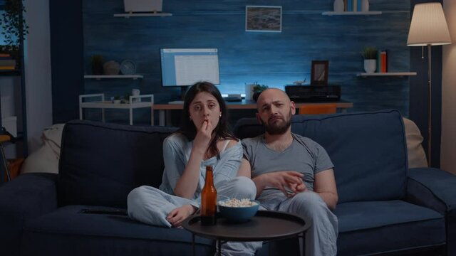 Sensitive couple watching drama movie on tv crying sitting on sofa eating popcorn late night. Persons in tears affected by film action, emotionally awestruck reacting to impressive astonishing moment