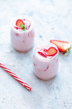 Two strawberry yogurt milk shakes with fresh strawberries on a table next to ingredients