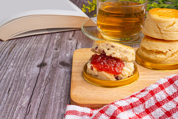 Scones traditional English delicious freshly baked homemade with strawberry jam and served on a wooden tray with a teacup. Side view. Dessert, beverage, and relaxation concept