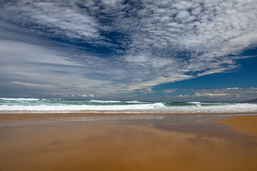 Fototapeta na wymiar Landscape sandy beach with a beautiful series of cloud patterns and types of reflections on the beach and surf waves on the east coast of Australia.