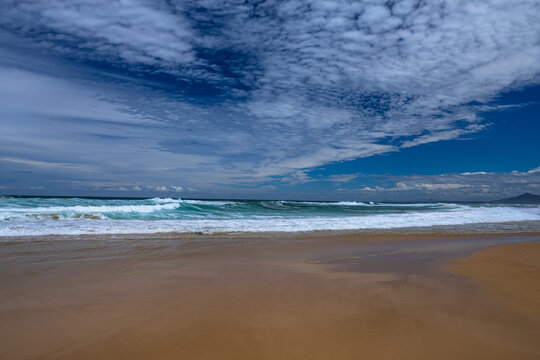 Landscape sandy beach with a beautiful series of cloud patterns and types of reflections on the beach and surf waves from the bright afternoon sunlight on the east coast of Australia.