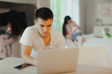 Young father works on laptop while his wife looks after child.