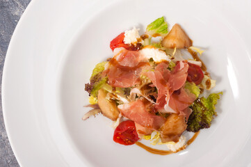 salad with jamon and vegetables on a white plate. Top view
