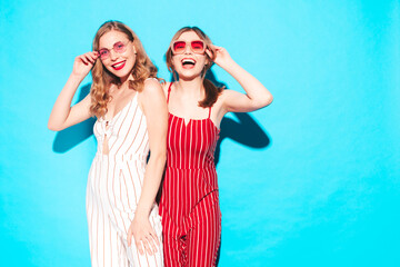 Two young beautiful smiling hipster female in trendy summer overalls clothes. Sexy carefree women posing near blue wall in studio. Trendy and positive models having fun. Cheerful and happy