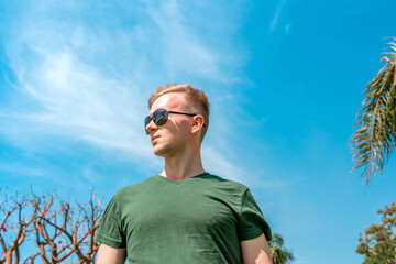 Portrait of a young man wearing sunglasses stands against a blue sky