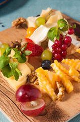 assorted cheese on a wooden Board with berries and walnuts