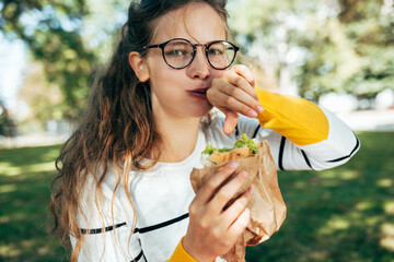 Portrait of a student female has a delicious lunch with a sandwich outdoors. A blonde young woman...