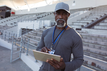 Portrait of african american male coach holding clipboard standing in the stadium