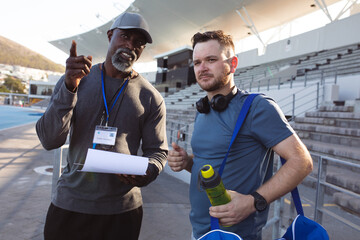 African american male coach instructing caucasian male athlete with prosthetic leg in the stadium