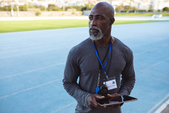 African american senior male coach holding digital tablet standing in the stadium
