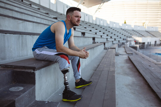Caucasian male athlete with prosthetic leg sitting on the seats in the stadium - Powered by Adobe