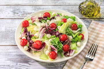 The Mediterranean diet. Healthy food composition with salad with herbs, cherry tomatoes, mozzarella and olive oil on a white plate with fork on a wooden background. The concept of simple healthy food