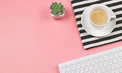 flat lay of coffee cup on black and white stripes cloth with computer keyboard and cactus in plant pot  on pink background with copy space.