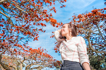 Young brunette girl against the sky and a blooming tree with red flowers, Los Angeles, Calfiornia