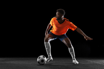 Young African football soccer player playing isolated on black background. Concept of sport, movement, energy and dynamic.