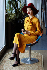 girl in a cafe with a cup of coffee and a hat.portrait of sensual young girl wearing floppy hat and blouse with bow. Beautiful brunette woman in cafe holding cup of coffee