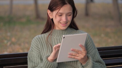 Student girl studying with tablet computer outdoors. Freelancer works online. Young woman works on a tablet in the park on a bench. A girl using a digital tablet prints messages on a city street.