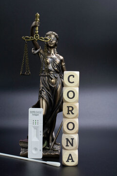 Justitia mit COVID 19 Schnelltest und Holzwürfel. Das Wort Corona steht auf den Würfeln