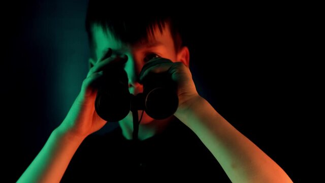 boy, guy 7-9 years old, stalker looks through black binoculars in the dark, spies, tracks down the secrets of private life, the concept of surveillance, people observation