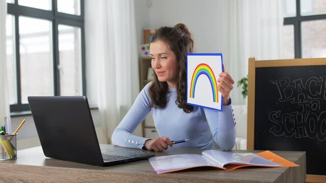 distant education, primary school and teaching concept - female teacher with laptop computer and picture of rainbow having online class at home