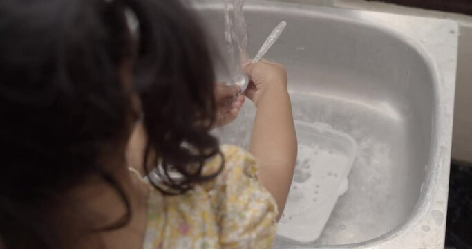 4K little Asian girl (back) (4 years old) learning how to wash a spoon by herself, homework, learning and training of kid Ef (Executive Functions), child learning concept.