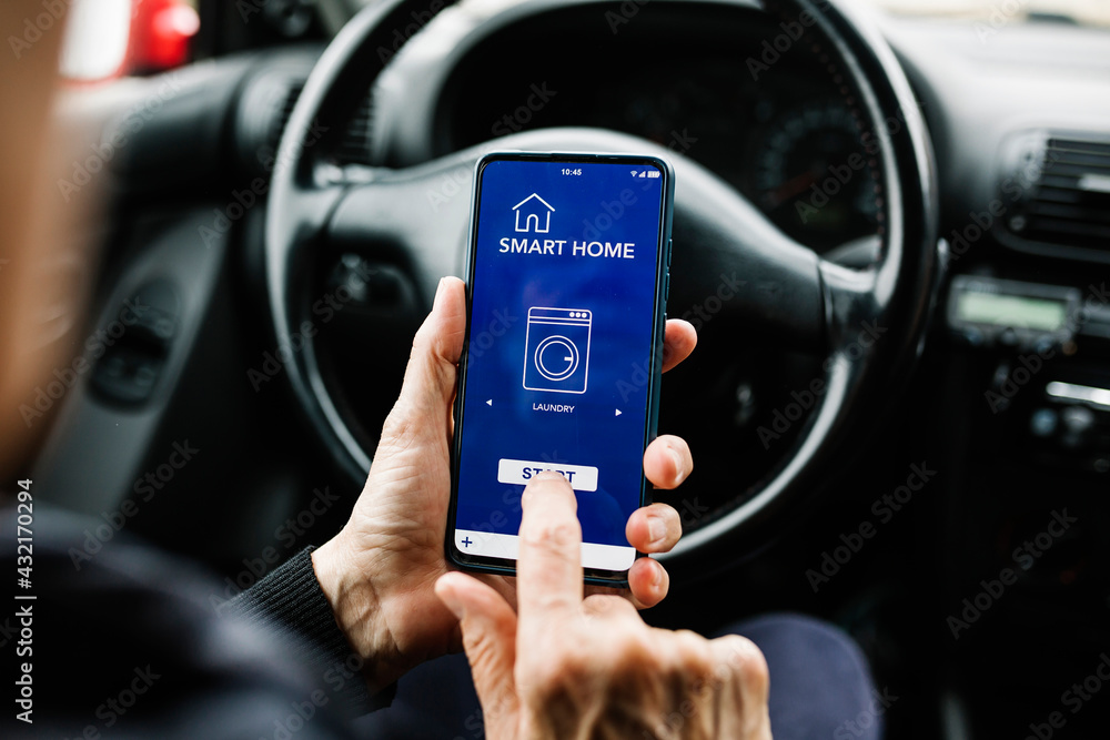 Wall mural crop anonymous person sitting on driver seat in car and using mobile phone with smart home app on sc