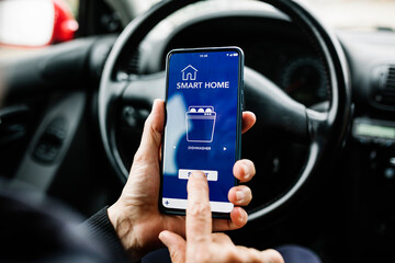 Senior woman sitting on driver seat in car and using mobile phone with smart home app on screen while programming the dishwasher remotely - Internet of things (IOT) concept