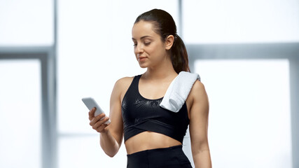 young sportswoman with towel looking at smartphone in gym.