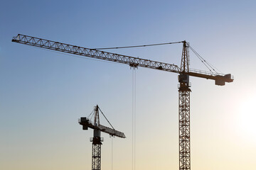 Construction cranes on blue sky and sunrise background. Housing construction in city