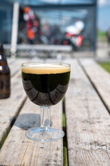 Glass of dark strong belgian beer served on outdoor terrace with green grass meadow on background