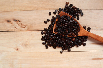 Coffee beans in wooden spoon with copy space isolated on wooden background closeup.