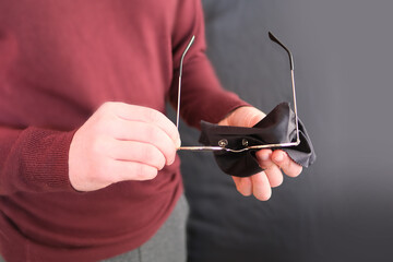 young man wipes a special black napkin glass round glasses in thin frames, the concept of myopia, vision, human health