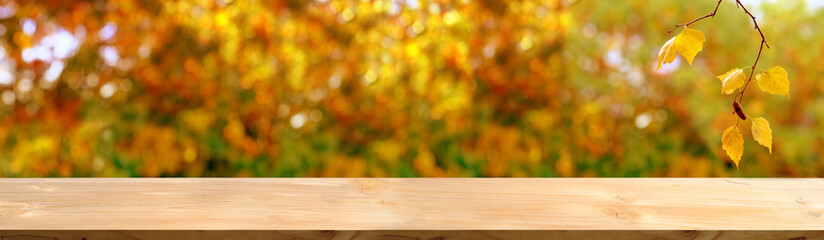 Naklejka na ściany i meble wooden table in the garden, beautiful blurred natural landscape in the background, long panorama, the concept of a cozy autumn mood, blank for the designer