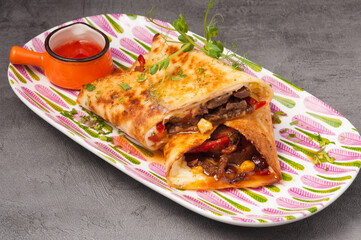 Mexican burrito with beef and vegetables and hot sauce